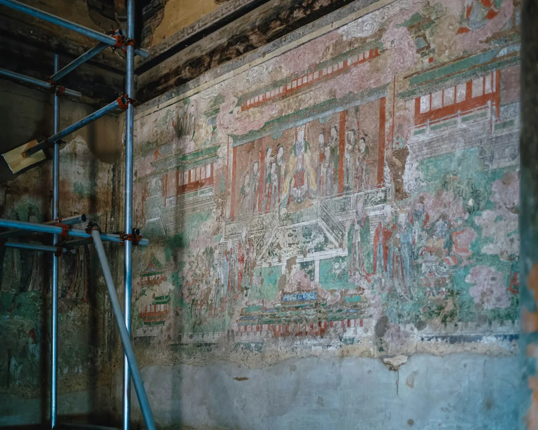 Muro con pintura mural antigua parcialmente perdida, con andamio tubular delante y zonas de enlucido desprendido